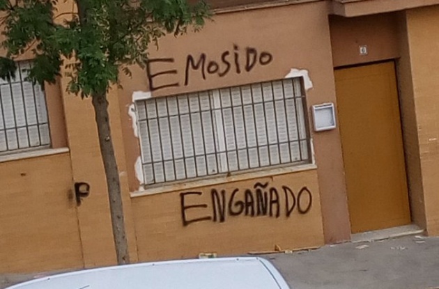 Meme: pintada en una pared que dice E MOSIDO ENGAÑADO, con la ventana enrejada llena de papeles en medio